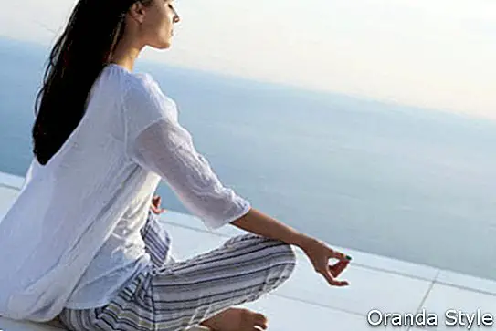 mlada ženska vadi meditacijo joge ob sončnem zahodu s pogledom na ocean v ozadju