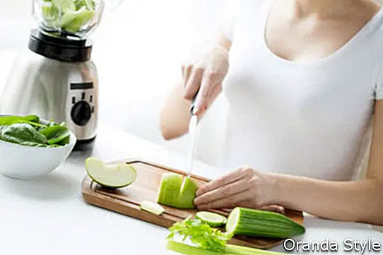 mlada ženska z mešalnikom sesekljano zeleno zelenjavo za detox shake ali smoothie doma