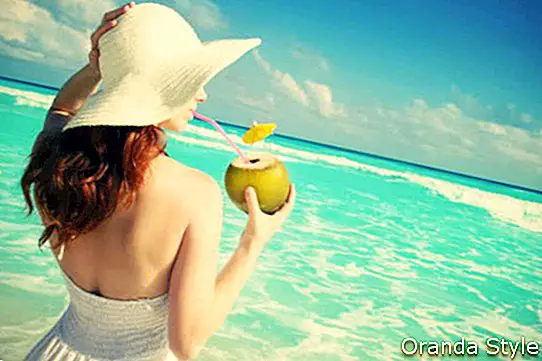 Женщина смотрит на океан и пьет кокосовую воду