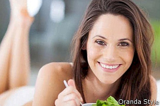 glückliche junge Frau, die grünen Salat auf Bett isst