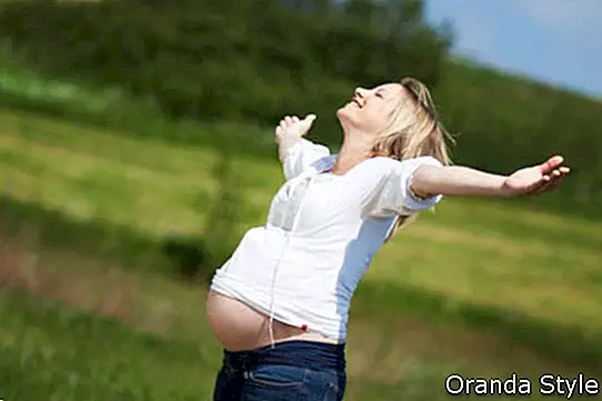 Щастлива бременна жена с разперени ръце, наслаждавайки се на слънчева светлина на поле