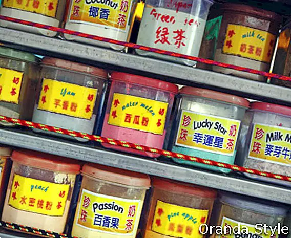 Filas de coloridos contenedores que contienen extracto de alimentos saborizantes en polvo en el estante de un puesto callejero chino