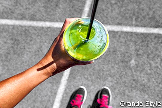 Die grüne Smoothiefrau, die Plastikschalenfrühstücksmahlzeit zum Mitnehmen trinkt, um Morgenlauf auf Stadtstraßen nachzulaufen