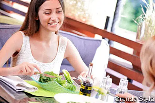 Naeratav brünett istub kohvikus koos oma armsa sõbrannaga ja sööb salateid