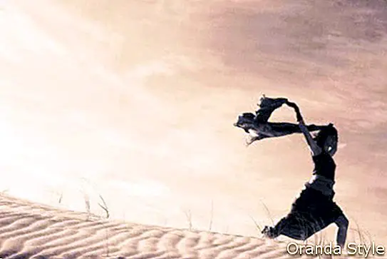 Siluet seorang wanita memegang syal yang bertiup di bukit pasir