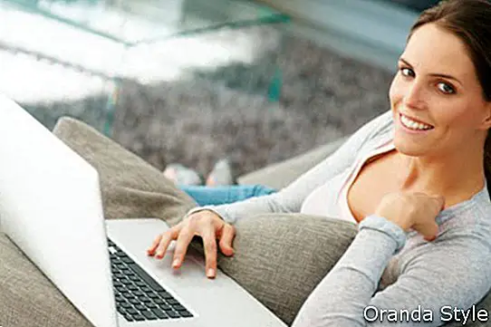 sonriente mujer joven con laptop en su sala de estar