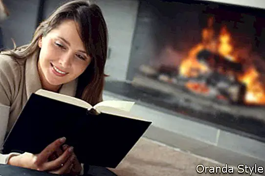 kvinne som leser bok ved siden av en peis
