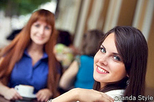 две приятелки, пиещи кафе на закуска в кафене на открито