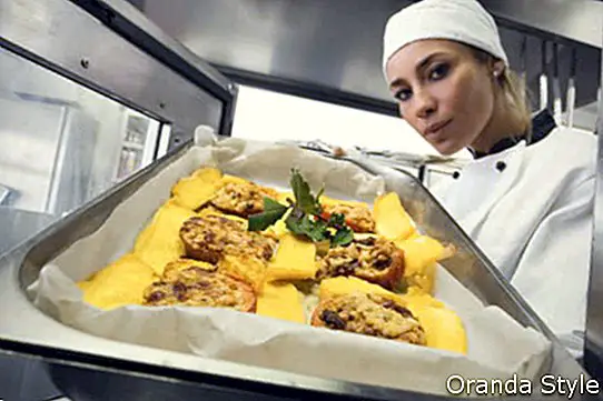 Mediados de mujeres adultas chef poner bandeja para hornear en el horno