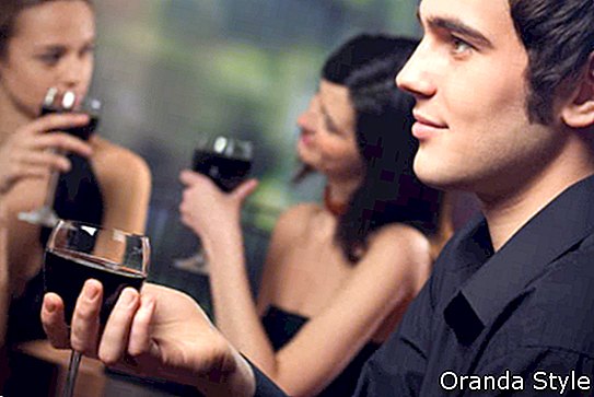 Ung kjekk mann med et glass rødvin og to attraktive kvinner