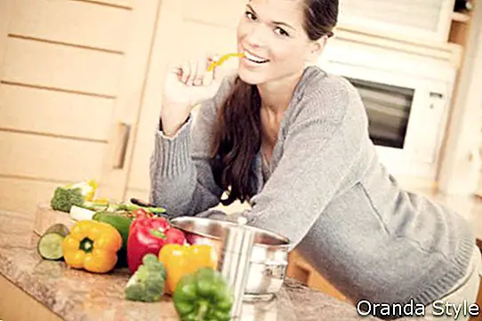 Šypsosi jauna moteris, valgydama papriką virtuvėje