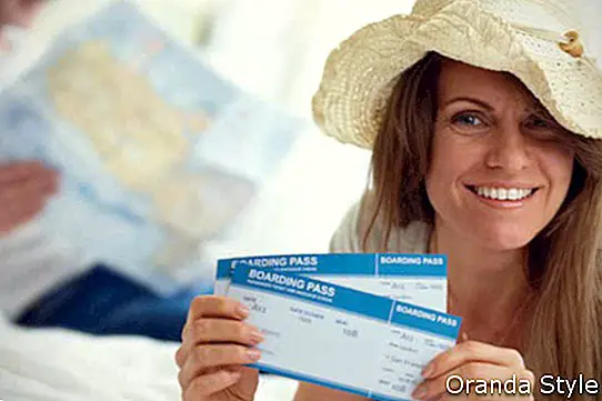 Senang wanita mengenakan topi menunjukkan tiket penerbangan
