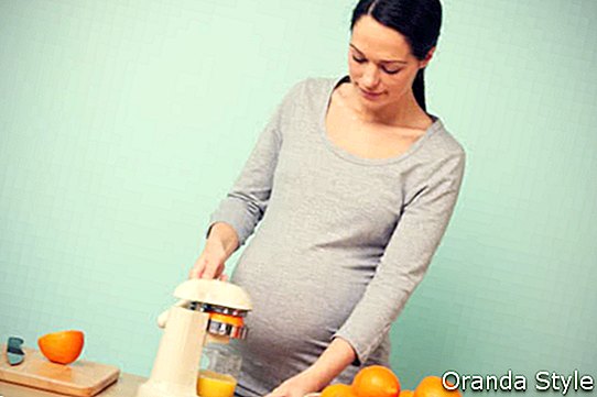 Mujer embarazada en su cocina preparando zumo de naranja recién exprimido