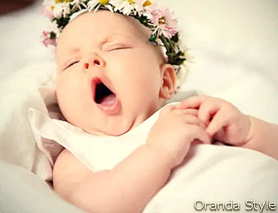 תינוקת מפהקת על רקע בהיר עם זר פרחים על ראשה