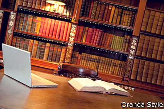 Лаптоп и книга лежат на бюро в класическа библиотека