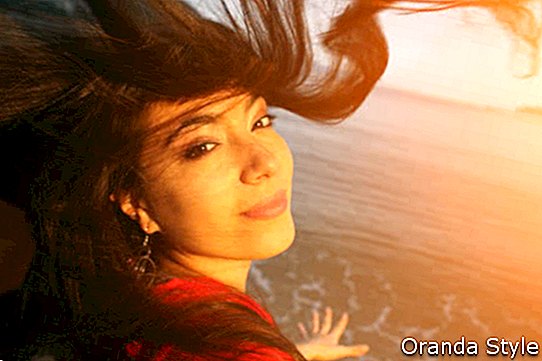 Jauna skaista sieviete ar lidojošiem matiem pludmalē pie saulrieta