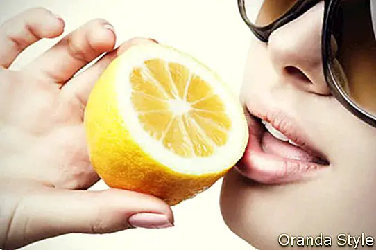 Naine päikeseprillidega, kes sööb sidrunit