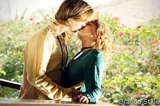 Joven pareja besándose en el balcón de una casa tropical
