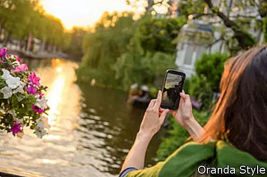 Eine touristische junge Frau in Amsterdam fotografiert einen wunderschönen Sonnenuntergang auf einer Brücke