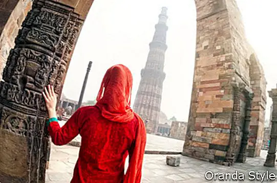 Raudono kostiumo moteris žvelgia į Qutub Minar bokštą Delyje