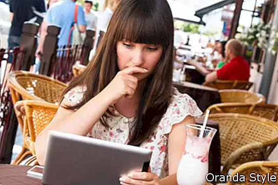 Trauriges Mädchen in einem Café, das eine Tablette untersucht