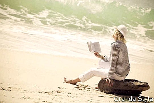 אישה עם כובע קורא ספר על החוף