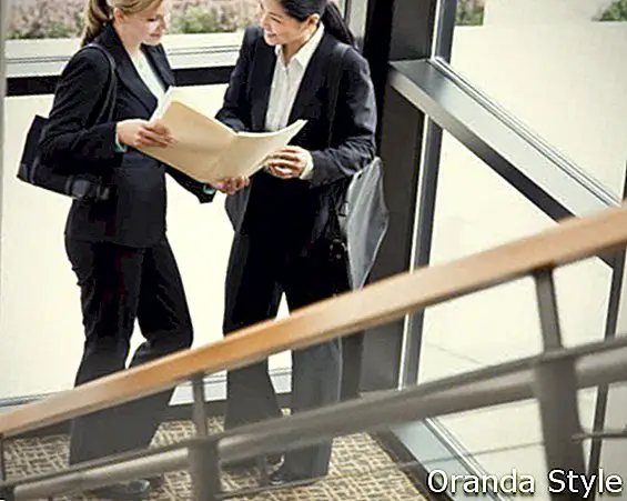 Жени колеги преглеждат файлове заедно в ъгъла на офис сградата