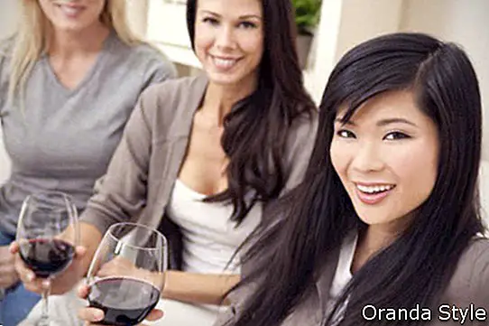 tři krásné mladé ženy přátelé doma pití červeného vína společně