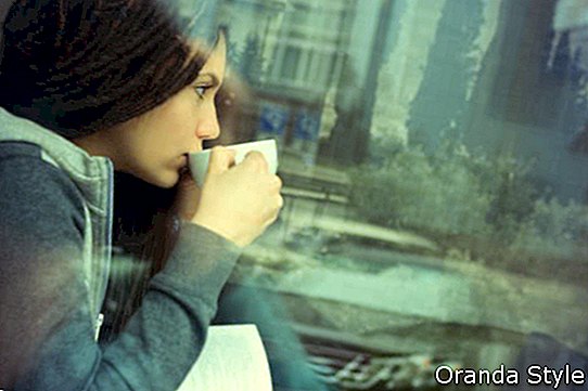 Млада жена, пиеща кафе и четеща книга, седнала на закрито в градското кафене