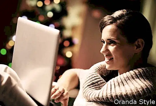 אישה צעירה מאושרת, עובדת על מחשב נייד מול עץ חג המולד
