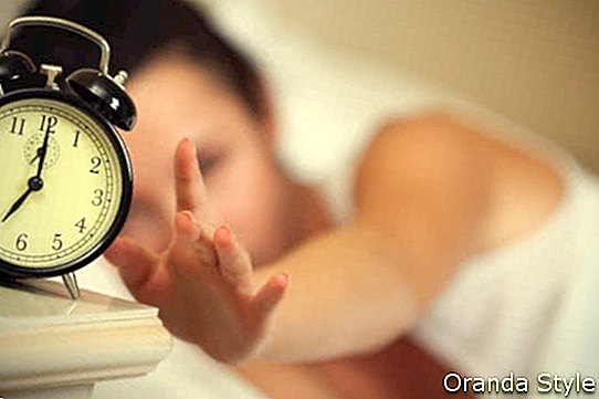 אישה שוכבת במיטה מכבה שעון מעורר בבוקר בשעה 7 בבוקר
