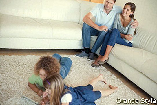 Niños que usan una tableta mientras sus felices padres están mirando en su sala de estar