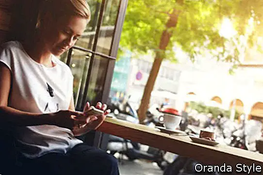 Nuori upea nainen juttelee älypuhelimellaan rentoutuessaan kahvilassa kävellen kesäviikonlopun aikana