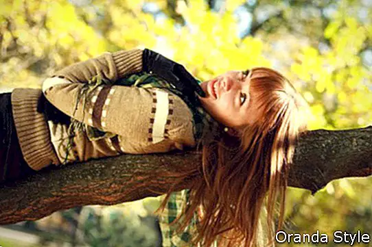 draußen Porträt des lächelnden Mädchens des Herbstes, das auf Baum liegt