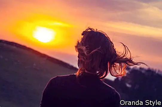 Молода жінка, милуючись заходом сонця над полями