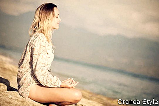 Mujer sentada en posición de loto sobre roca junto al mar