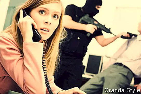 Retrato de empresaria horrorizada presionando los botones del teléfono mientras terrorista amenazando a su colega en el fondo
