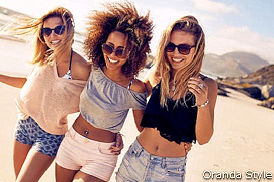 דיוקן של שלוש חברות צעירות שהולכות על חוף הים ומביטות במצלמה צוחקת
