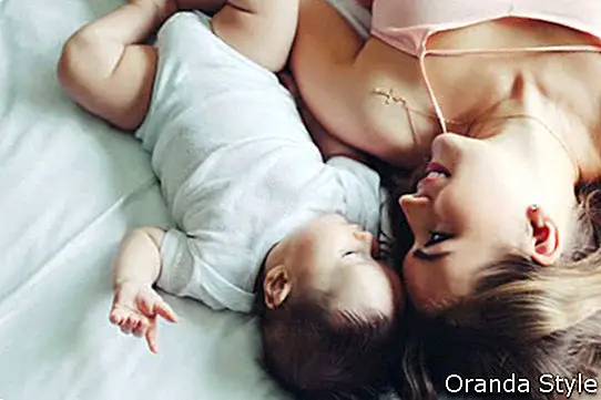 Retrato de hermosa mamá jugando con su bebé de 4 meses en el dormitorio