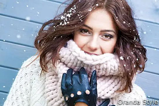 Зимен портрет на млада красива брюнетка, носеща трикотажен снуд, покрит в сняг