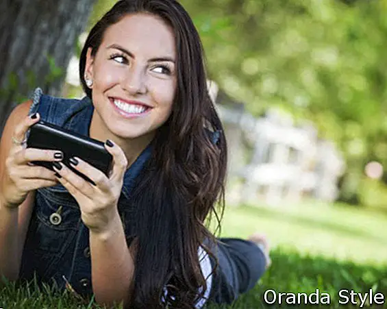 Atraktivní šťastné smíšené rasy mladá žena textových zpráv na její mobilní telefon