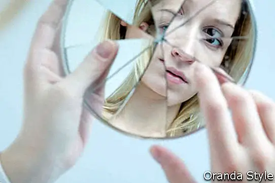 Nesigurna lijepa mlada žena koja drži razbijeno ogledalo