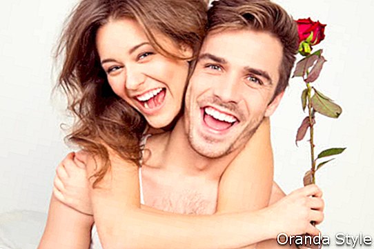 Munter ungt par forelsket omfavne på soverommet med rose