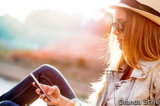 Mensajes de texto de mujer hipster en puesta de sol junto al mar