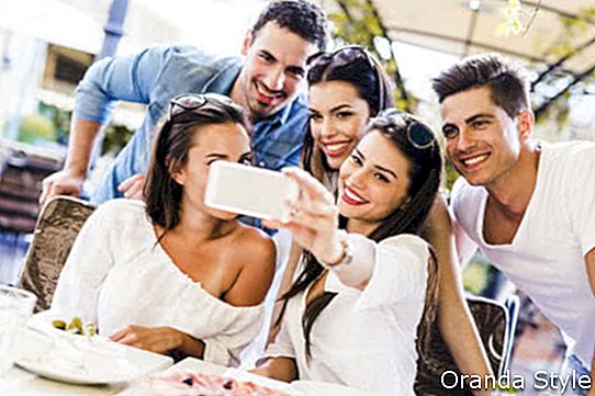 Csoport fiatal gyönyörű emberek ül egy étteremben, és vesz egy selfie mosolyogva
