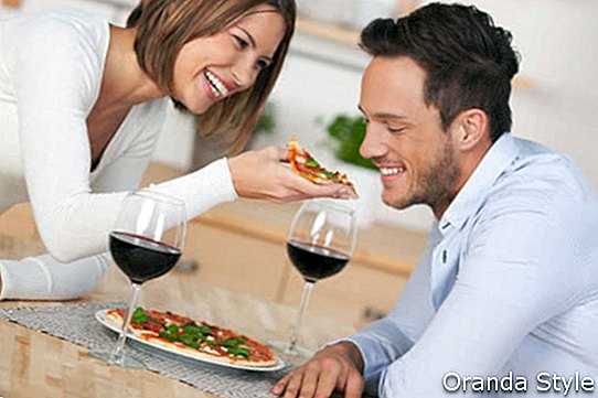 Щастлива млада двойка яде пица с червено вино в кухнята