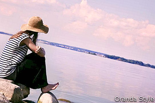 امرأة أنيقة وحدها يجلس على ساحل الحجر والنظر في البحر