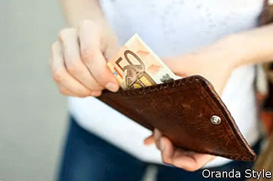 Chica saca un billete de cincuenta euros de una billetera de cuero marrón en la calle
