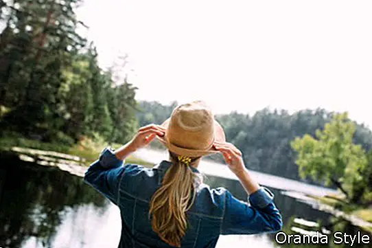 jauna sieviete salmu cepurē, kas stāv pie ezera mežā