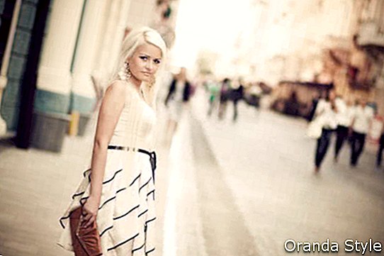 Красива млада жена в бяла рокля, която държи чанта на улицата